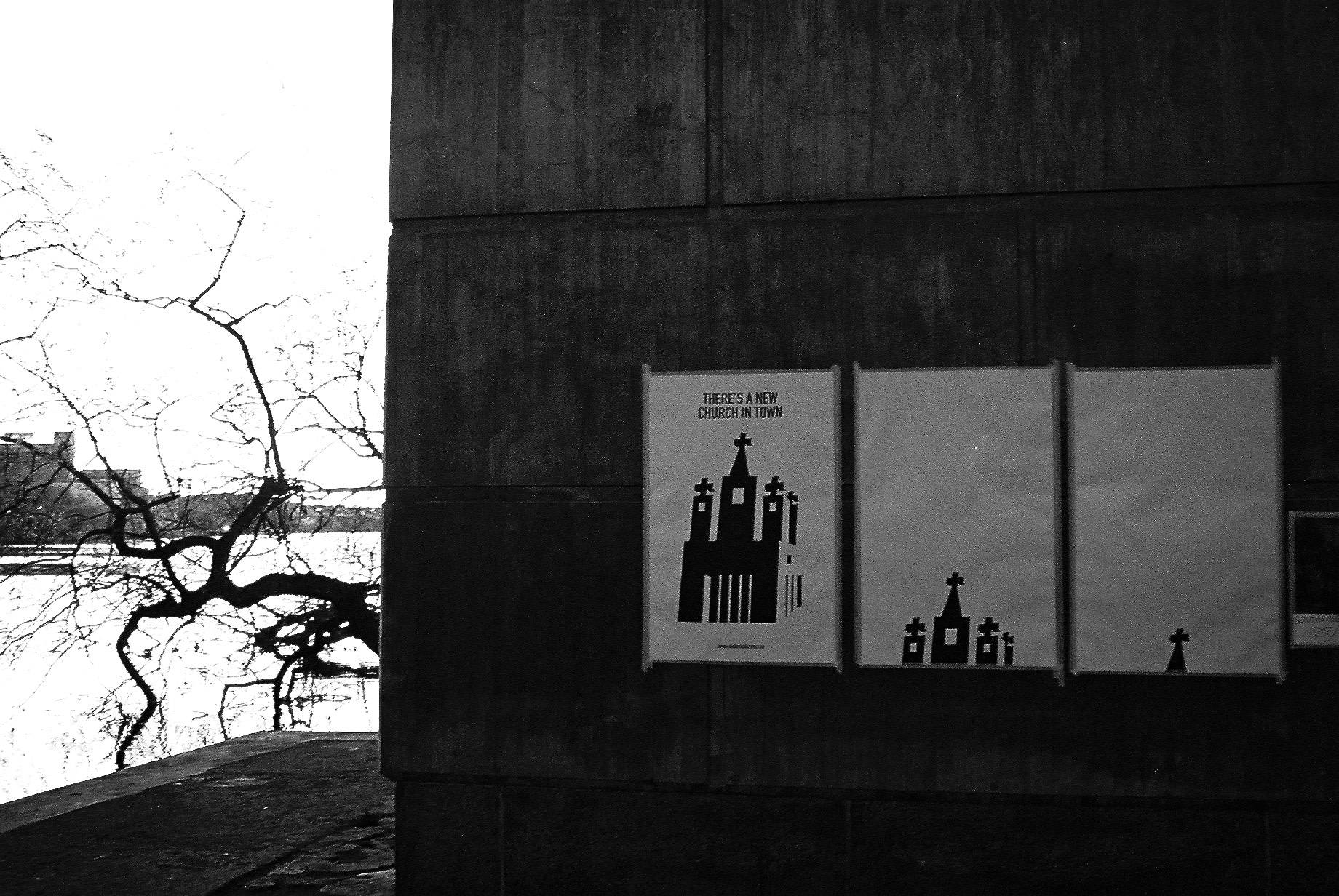 three related posters on the concrete column where the first one reads 'there's a new church in town'