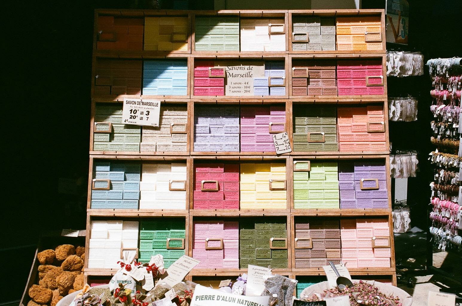 soap bars on display stacked on top of each other inside wooden crates that are also stacked, soap bars are grouped by colours that range between various pastel tones of reds, greens, browns and blues, as well as white