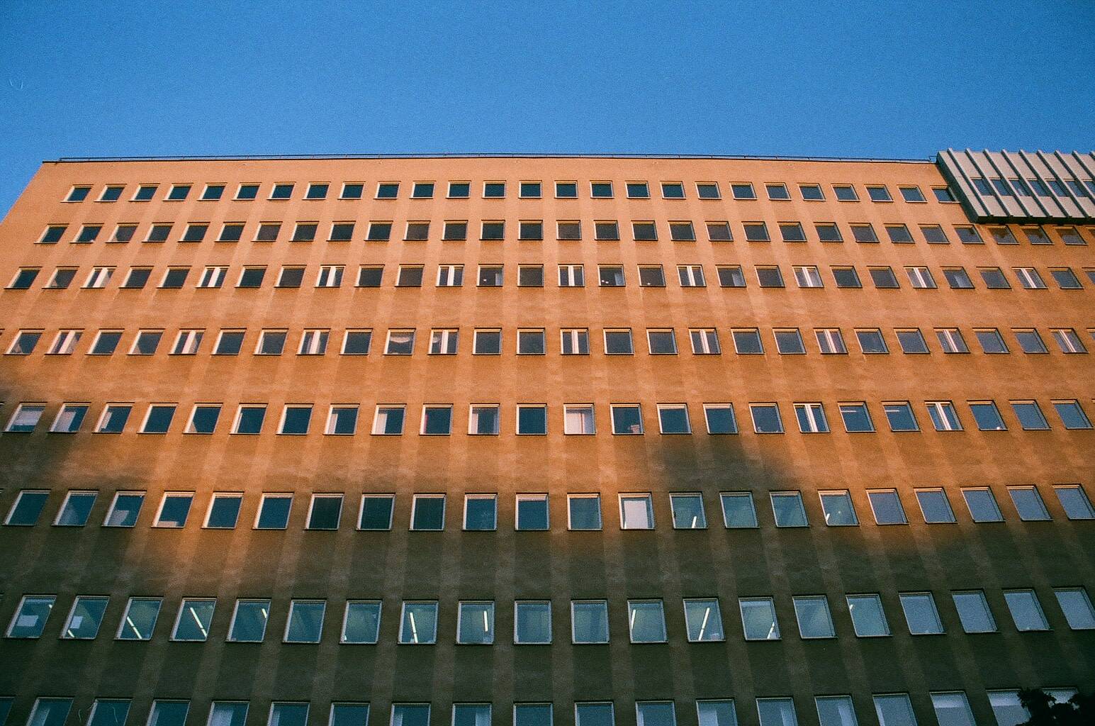side view of a large brown building that has symmetrically distributed small rectangular windows under the blue sky