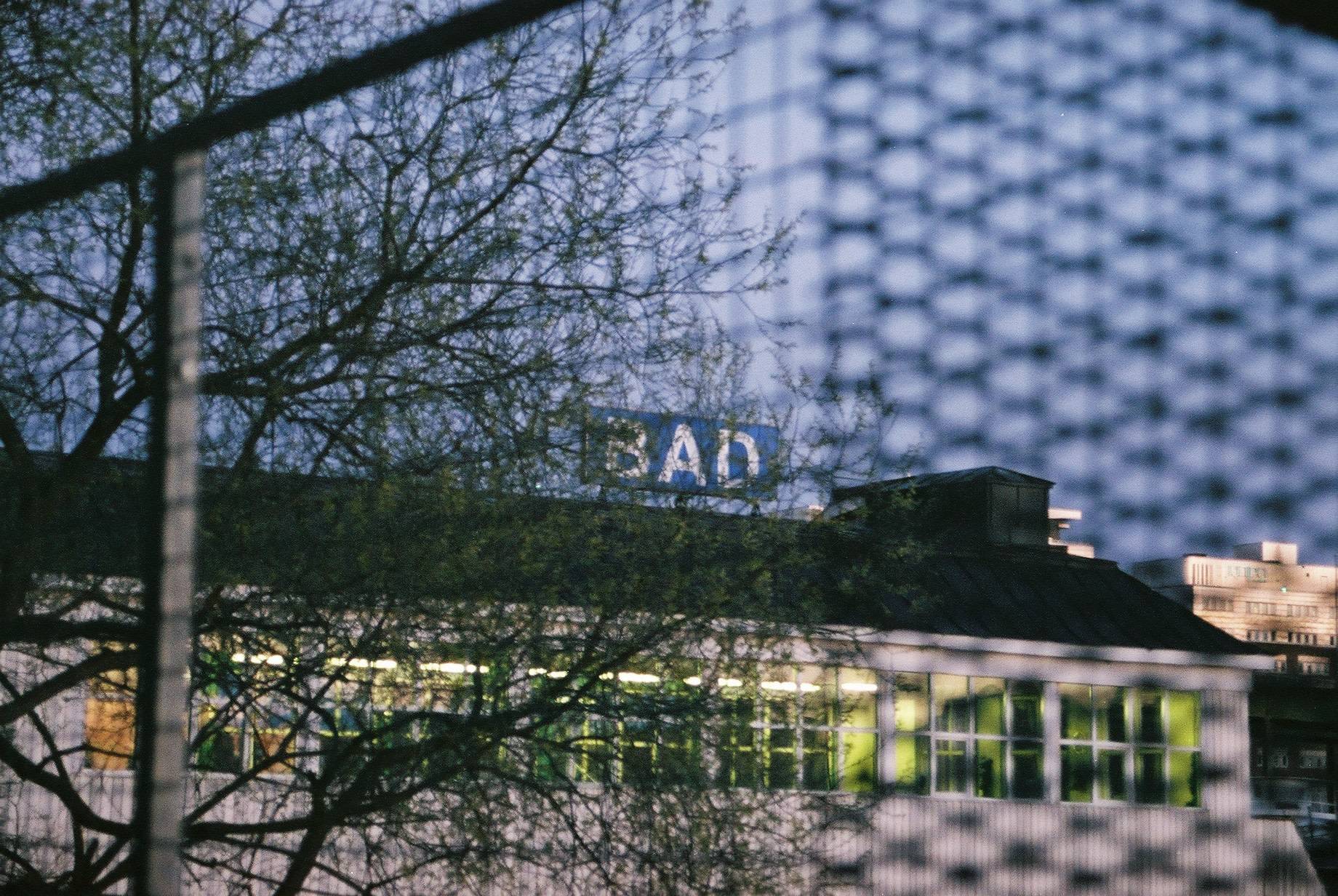 building seen through metal woven fence, where the sign on the building reads 'bad'