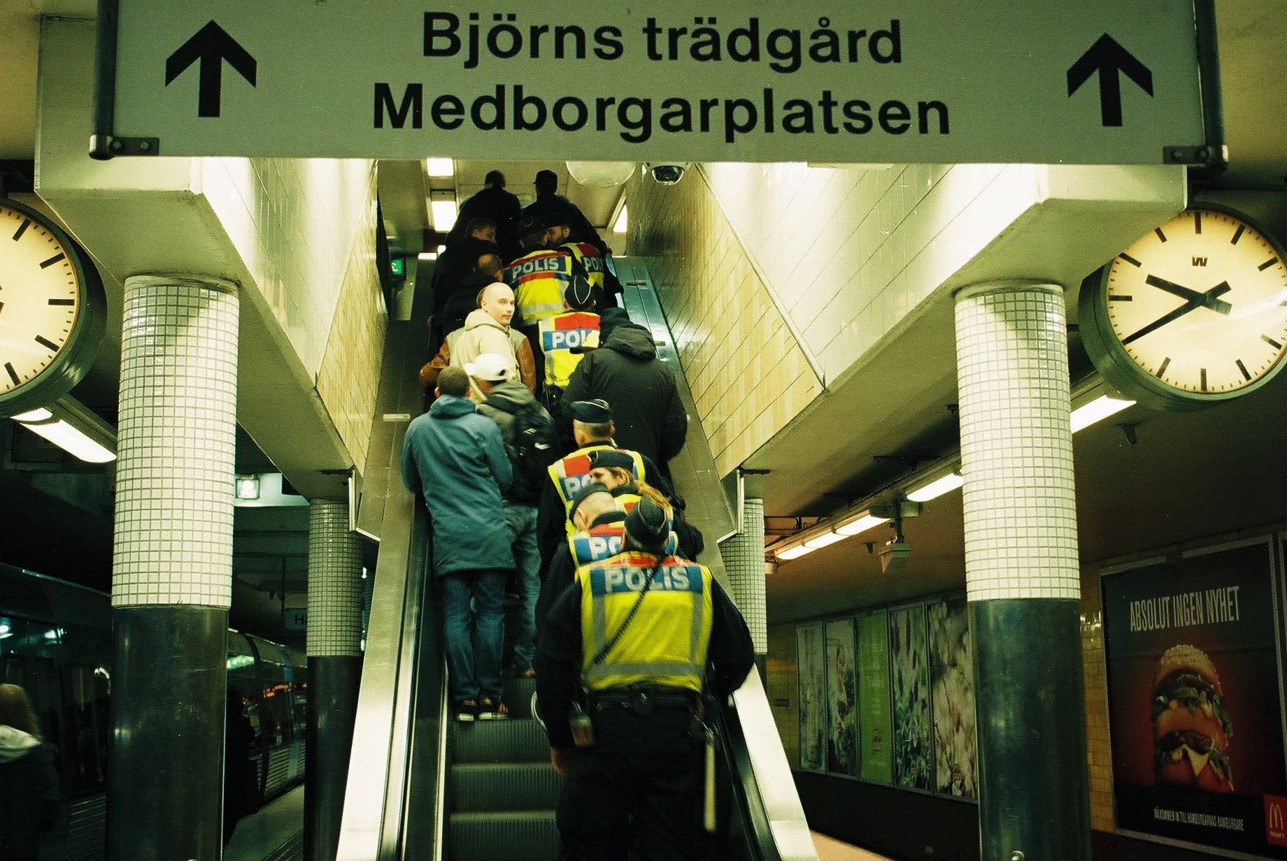 a group of people and police taking the escalator up with one man among the group looking into the camera