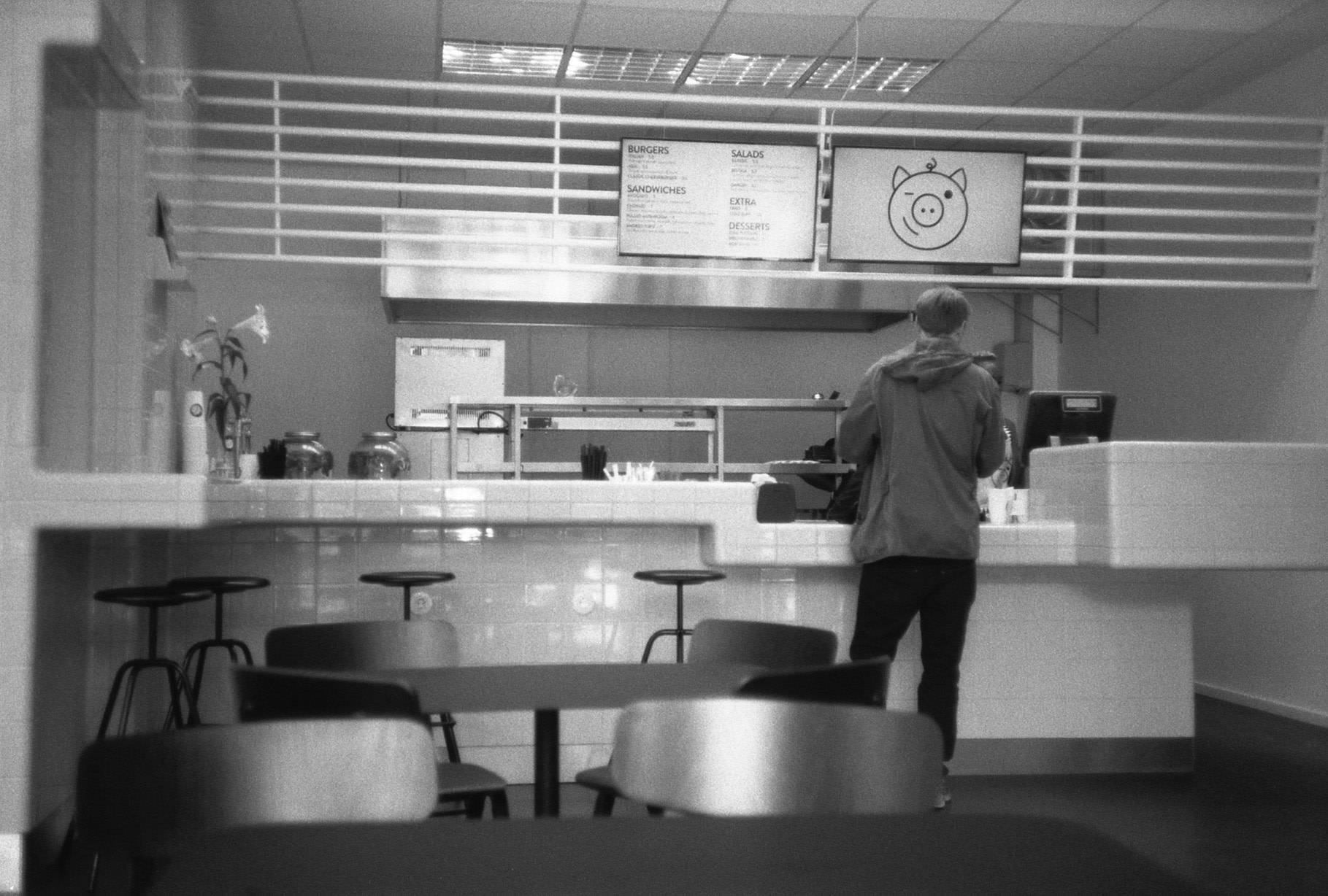 interior of a restaurant where a person seen from behind is ordering at the counter, the sign above the counter has a cartoon pig face
