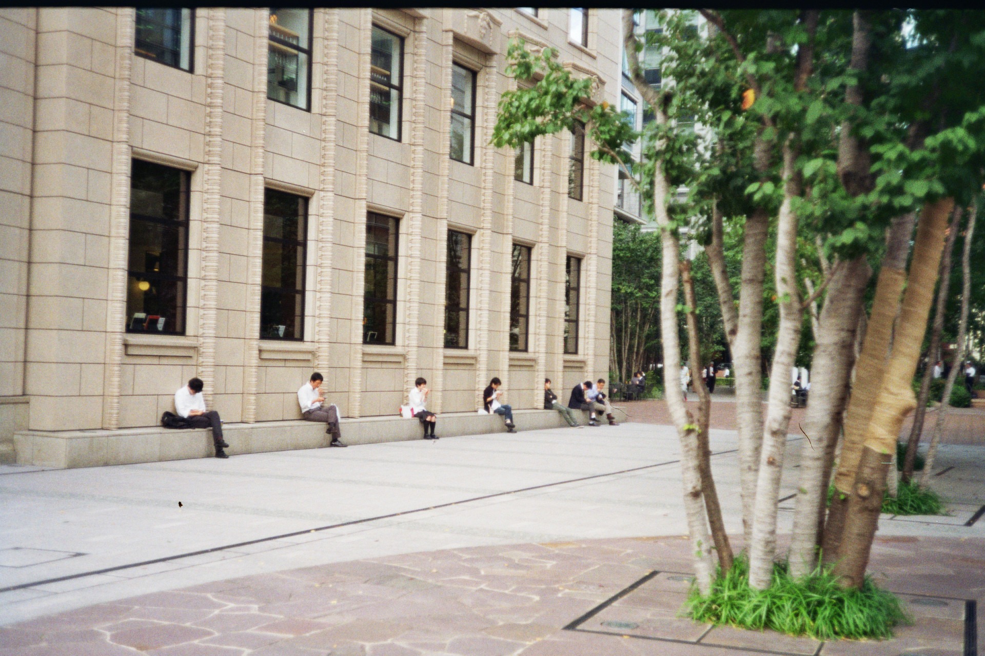 people sitting next to a building and eating their lunch, they sit almost equidistant from each other, a person below each window of the building
