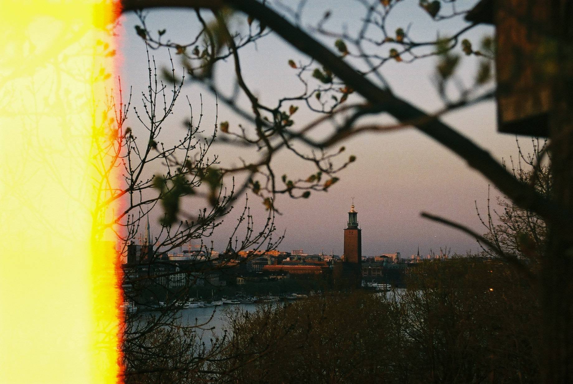 city hall of Stockholm seen over the river through branches, there is a yellow red band on the left side where the film is burnt
