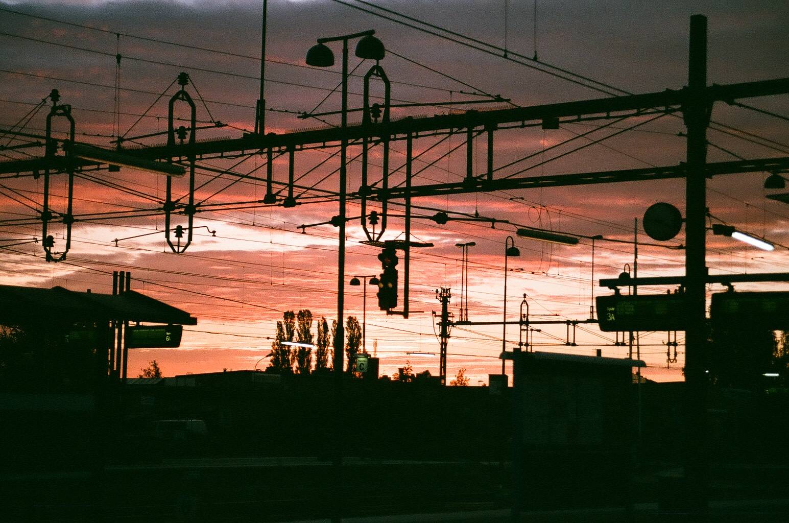 cloudy red sky visible through the electrical poles and wires of the train station