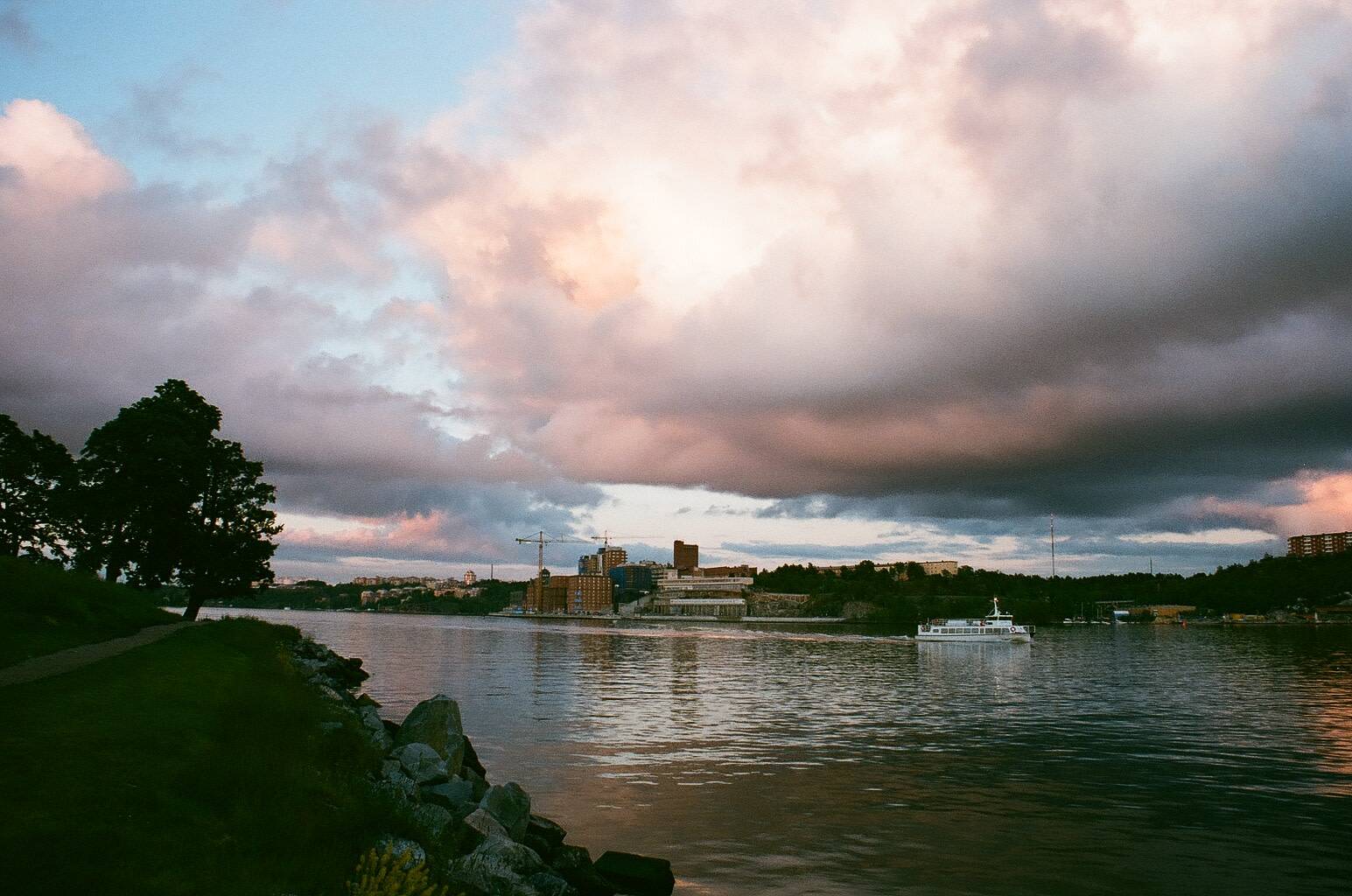 view of the landscape and urban area around a small bay that a ferry is arriving where the sky is covered with enormous clouds with pink hues