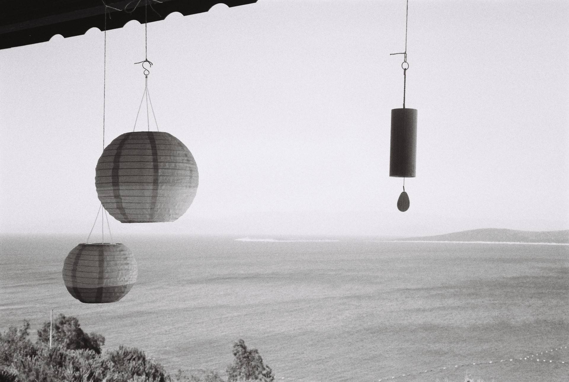 two paper lanterns and a wind chime hanging from the edge of the roof, sea and the clear sky merge in the background