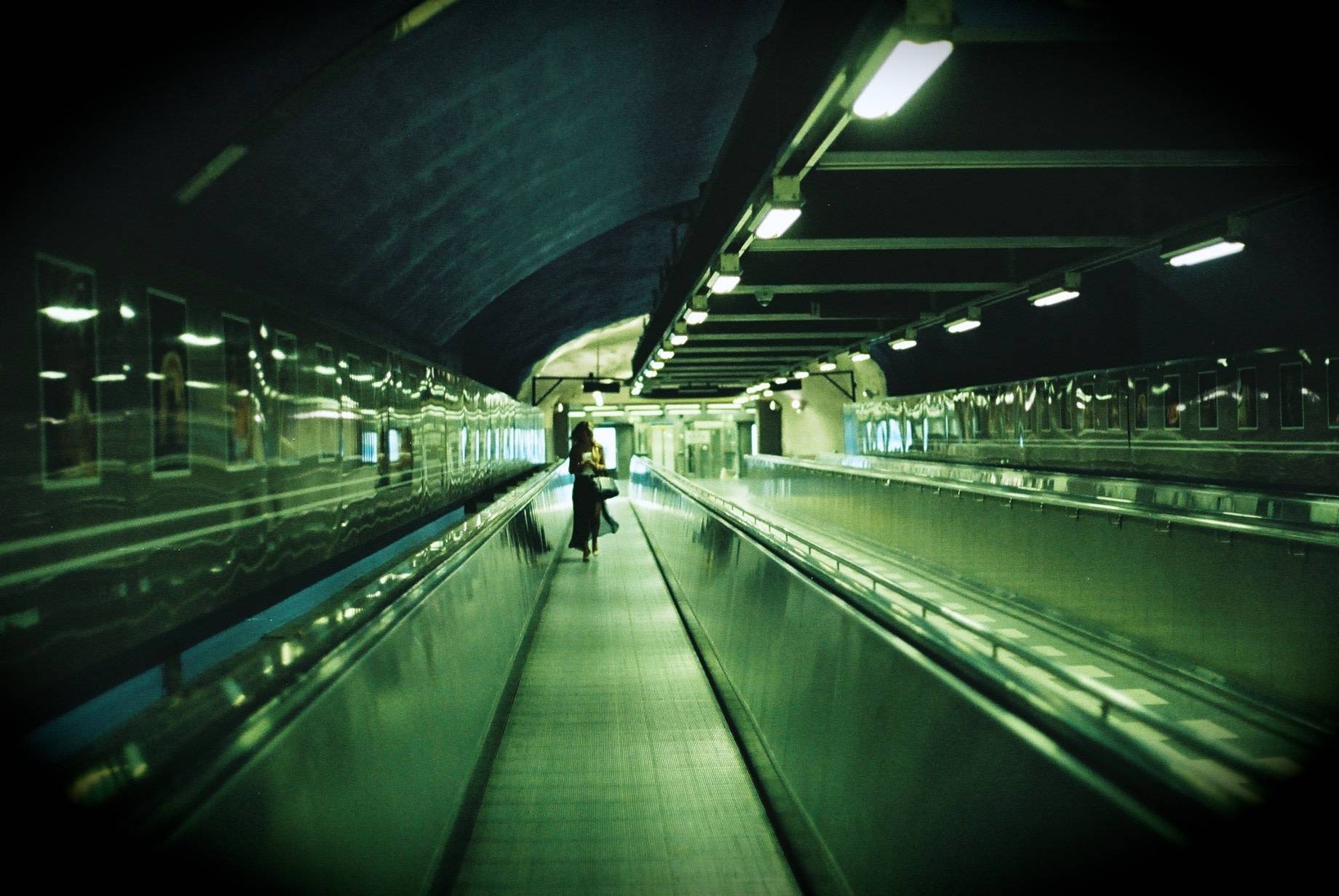 woman walking on a moving walkway in a subway station and looking at her phone 